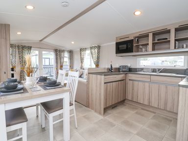 A dining area with a set table and a kitchen with wooden cabinets and a microwave at Lazy Dayz Lodge in East Heslerton near Malton