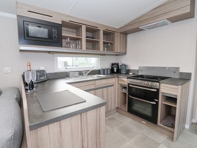 A kitchen with wooden cabinets a microwave an oven a sink and various kitchen appliances at Lazy Dayz Lodge East Heslerton near Malton
