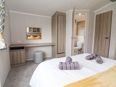 A bedroom with a bed with towels on it a desk with a stool a wardrobe and an open door leading to a bathroom at Lazy Dayz Lodge East Heslerton near Malton