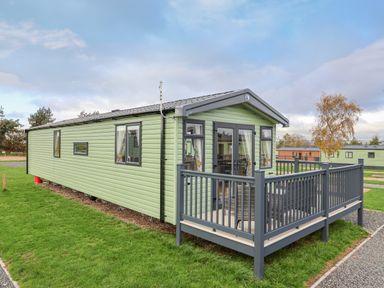 A green mobile home with a small fenced porch on a grassy area at Lazy Dayz Lodge East Heslerton near Malton