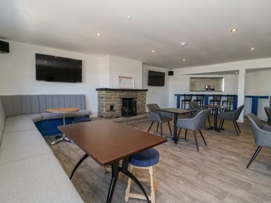 A lounge area with tables chairs a stone fireplace two wall mounted TVs and a seating bench at Lazy Dayz Lodge in East Heslerton near Malton
