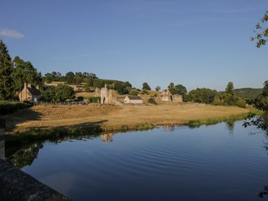 A river with a grassy bank and old stone buildings in the background in a rural area