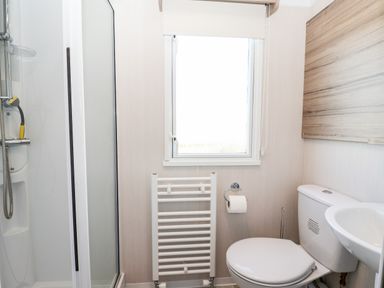 A bathroom with a shower, toilet, sink, towel radiator, and a window at Lazy Dayz Lodge in East Heslerton near Malton