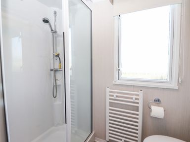 A bathroom with a shower enclosure a radiator a window and a toilet roll holder at Lazy Dayz Lodge in East Heslerton near Malton