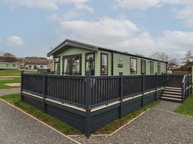 A green mobile home with multiple windows and a black railing deck on a gravel and grass lot at Lazy Dayz Lodge in East Heslerton near Malton