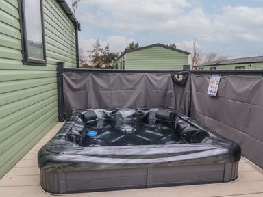 An outdoor hot tub on a deck enclosed by gray privacy screens and adjacent to green mobile homes at Lazy Dayz Lodge in East Heslerton near Malton