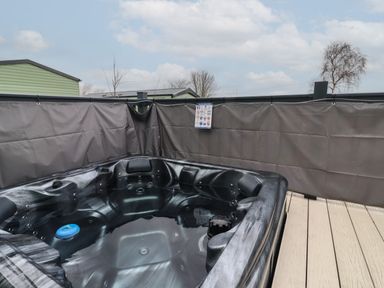 An outdoor hot tub on a wooden deck with privacy screens around it at Lazy Dayz Lodge in East Heslerton near Malton