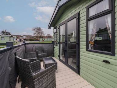 An outdoor seating area with black wicker chairs and a table on a deck outside a green mobile home at Lazy Dayz Lodge in East Heslerton near Malton