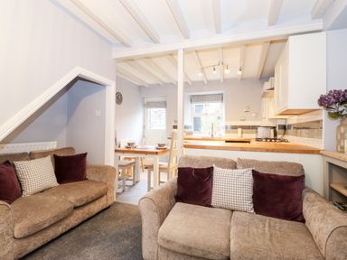 A living room with two sofas and pillows next to a dining area with a wooden table and chairs and an open kitchen with wooden countertops at Fell View in Ambleside