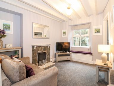 A living room with a stone fireplace television on a wooden stand and a window seat at Fell View in Ambleside