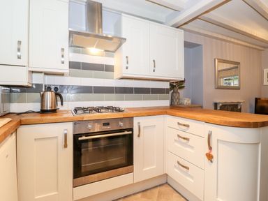 A kitchen with white cabinets, wooden countertops, a stainless steel oven, a gas stove, and a kettle at Fell View in Ambleside