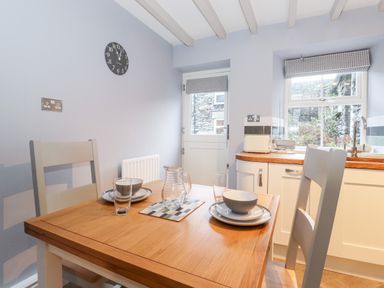 A kitchen with a wooden table set for two near a door and window with checked blinds at Fell View in Ambleside