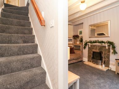 A carpeted staircase next to a living room with a stone fireplace sofa mirror and decorative greenery at Fell View in Ambleside