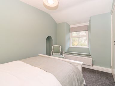 A bedroom with a bed, an armchair, a window with a roman shade, and a radiator at Fell View in Ambleside