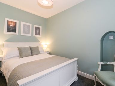 A bedroom with a white bed a bedside lamp framed pictures on the wall and a chair at Fell View in Ambleside