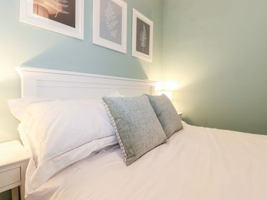 A bed with white bedding and two green pillows beside two bedside tables with lamps and three framed pictures on a light blue wall at Fell View in Ambleside
