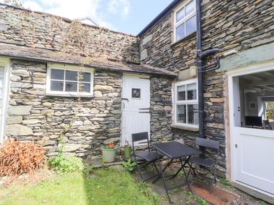 An outdoor stone patio area with a black metal table and two chairs next to a white door and window at Fell View in Ambleside