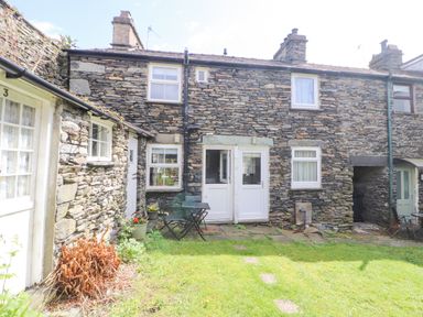 A stone house with white doors and windows with a small patio and garden at Fell View in Ambleside