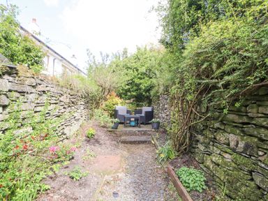 A narrow garden area with stone walls on both sides and outdoor chairs and table at the far end at Fell View in Ambleside