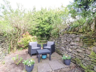 An outdoor patio area with two chairs a small table and potted plants surrounded by stone walls at Fell View in Ambleside
