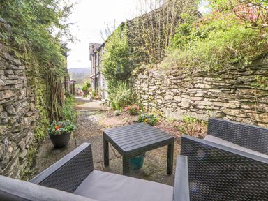 An outdoor seating area with two chairs and a table between stone walls and plants at Fell View in Ambleside