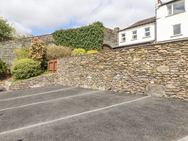 A parking area with marked spaces next to a stone wall and buildings with shrubs and greenery at Fell View Ambleside