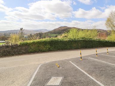 An empty parking lot with bollards and a stone wall covered with greenery with hills and trees in the background at Fell View in Ambleside