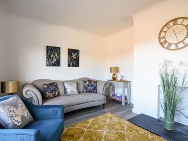A living room with a sofa armchair cushions side table wall clock and decorative plants at Hook Farm Cottage in Uplyme