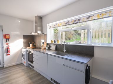 A kitchen with white cabinets a sink an oven washing machine and large window at Hook Farm Cottage in Uplyme