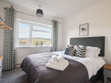 A bedroom with a bed with pillows and towels near a window with curtains at Hook Farm Cottage in Uplyme