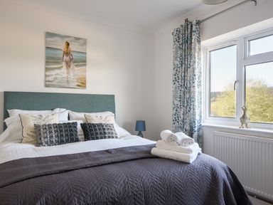 A bedroom with a bed with pillows and folded towels near a window with patterned curtains at Hook Farm Cottage in Uplyme