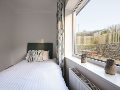 A bedroom with a bed with patterned pillows next to a window with owl decorations on the sill at Hook Farm Cottage in Uplyme