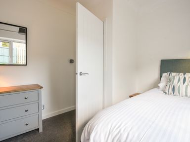 A bedroom with a bed, a dresser with drawers, a mirror, and an open door at Hook Farm Cottage in Uplyme