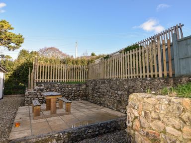 An outdoor paved seating area with wooden benches and table surrounded by stone walls and a wooden fence at Hook Farm Cottage in Uplyme