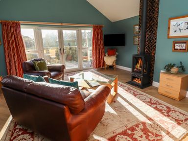 A living room with leather sofa and armchair glass coffee table wood burning stove and large windows at Summerseats Cottage in Alnwick