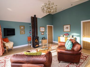 A living room with leather sofas a wood burning stove a glass coffee table and a chandelier at Summerseats Cottage in Alnwick