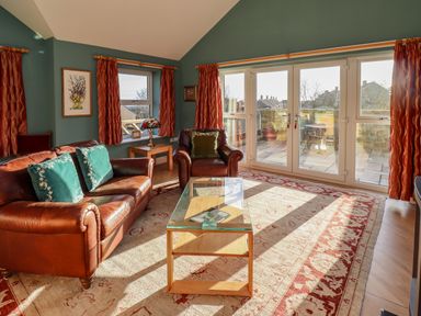 A living room with leather sofa and armchair glass coffee table and large windows at Summerseats Cottage in Alnwick