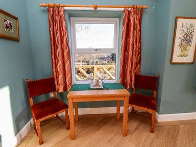 A wooden table with two chairs near a window with curtains and framed pictures on walls at Summerseats Cottage in Alnwick