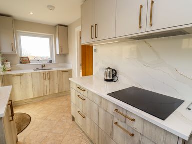 A kitchen with wooden cabinets white marble countertops a window and an electric stove at Summerseats Cottage in Alnwick