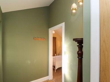 A hallway with green walls and a wooden coat rack leading to a bedroom with a white bed frame at Summerseats Cottage in Alnwick