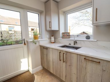A kitchen corner with a sink under a window and wooden cabinets at Summerseats Cottage in Alnwick