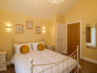 A bedroom with a white metal bed frame white bedding two round yellow pillows two white nightstands two doors wall mirror and framed botanical prints at Summerseats Cottage in Alnwick
