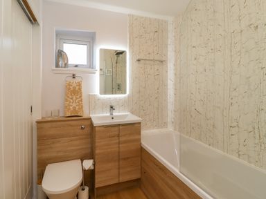A bathroom with a toilet sink wooden cabinets bathtub and a small window with a towel on a rail at Summerseats Cottage in Alnwick