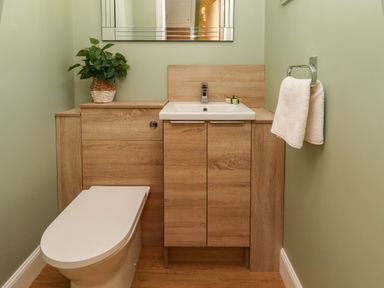 A small bathroom with a wooden cabinet, white sink, toilet, towel rack with a white towel, and a plant on the cabinet at Summerseats Cottage in Alnwick