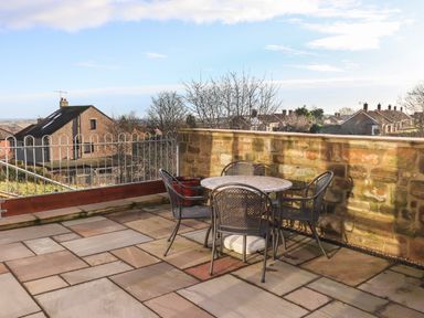 An outdoor patio with a round table and four chairs next to a stone wall overlooking houses