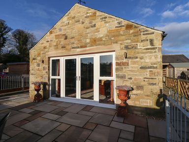 A stone exterior wall with white framed glass doors and windows with two planters on a paved patio at Summerseats Cottage in Alnwick