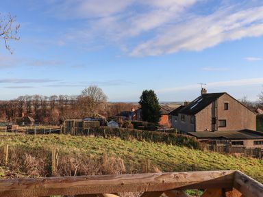 A view of grassy fields and houses with trees in the background at Summerseats Cottage in Alnwick