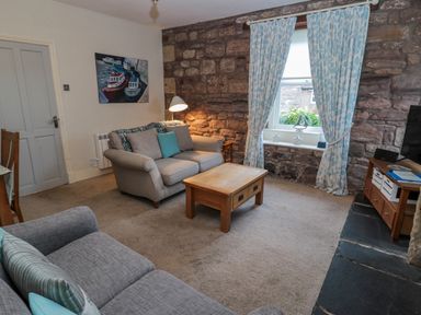 A living room with sofas a wooden coffee table and stone wall at The Haven in North Sunderland near Seahouses