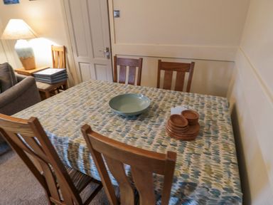 A dining table with a patterned tablecloth and wooden chairs in a room with a lamp and books at The Haven in North Sunderland near Seahouses