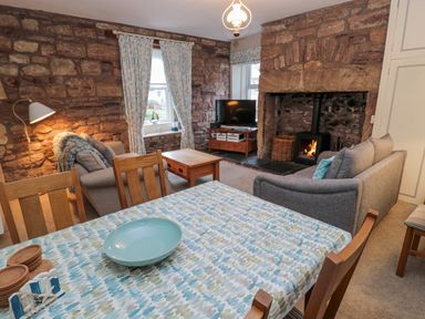 A dining table with a patterned tablecloth and a bowl in a living room with stone walls and a fireplace at The Haven in North Sunderland near Seahouses